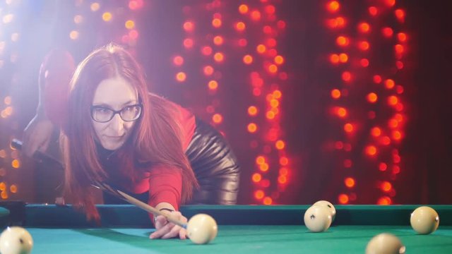 Billiard club. Concentrated ginger woman aiming and hitting the ball