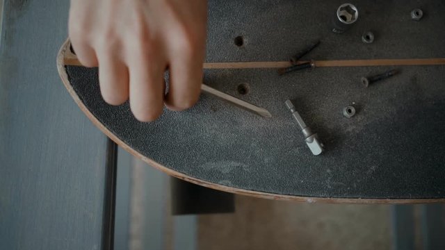 Top closeup view of male hands using alan key to unscrew bolts from skateboard. Uses special tools to disattach trucks. Concept teenager hobby or artisan activity