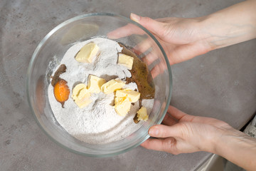 Kobiece dłonie trzymają misę z niewymieszanymi składnikami do wypieku ciasta w szklanej misce. Jajka, mąka, margaryna w szklanej misce trzymana przez kobiece dłonie.