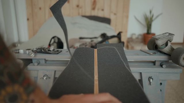 Soft focus slow motion cinematic shot of small personal workshop or garage where professional skateboarder in love with his sport lovingly regrips old longboard with new grip tape.