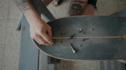 Skateboarder or longboarder unscrews bolts and screws from old board, to prepare deck to regripping. Artisan craft or handmade skill, do it yourself at home. Authentic hobby - Powered by Adobe