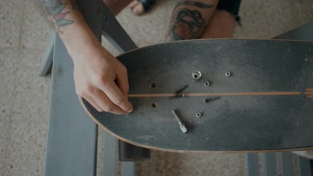 Skateboarder or longboarder unscrews bolts and screws from old board, to prepare deck to regripping. Artisan craft or handmade skill, do it yourself at home. Authentic hobby