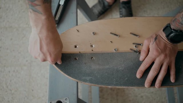 Authentic and beautiful cinematic shot of young man at skateboard workshop work on regripping old board. Small business personally works on small diy handmade project