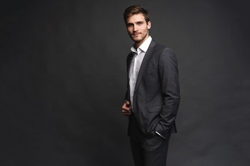 Portrait of a handsome young businessman dressed in suit isolated over gray background.