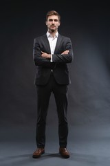 Full length portrait of a handsome young businessman dressed in suit isolated over gray background,...