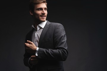 Perfect to the last detail. Handsome young businessman adjusting his sleeves while standing against gray background.