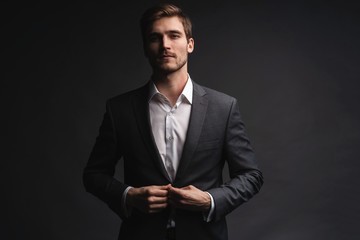 Portrait of serious handsome man in gray suit buttoning jacket