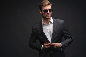 Stylish young man in suit and sunglasses. Business style. Office worker. Sexy man standing isolated over gray background