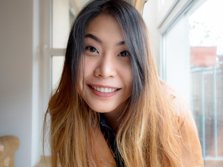A portrait of excited Asian young woman sitting at home and looking at camera with joy, happy face....