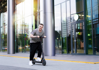 Attractive young man riding a kick scooter at cityscape background.