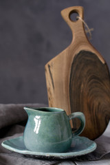 Natural handcrafted dishware. Wooden brown cutting board and ceramic blue cream jug with gray linen...