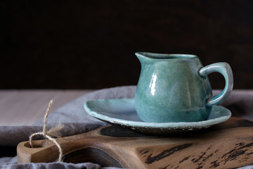 Natural handcrafted dishware. Wooden brown cutting board and ceramic blue cream jug with gray linen napkin. Country, rustic style