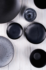 Set of porcelain handcraft  grey and black plates and  bowls on a white wooden table. Flat lay