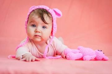 Cute Caucasian baby girl with a funny pink hat with ears and a pink teddy bear soft toy looking at the camera. Adorable infant model concept.