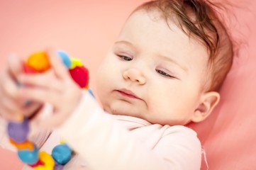 Cute Caucasian baby girl taking into her mouth a teething toy. First tooth concept illustrative image.