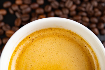 Grains of coffee and white cup of brewed coffee. Tasty foam on the surface of a delicious drink.