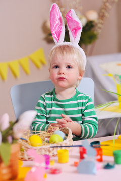 preparation for the celebration of Easter - baby boy paints eggs in yellow on the background of a festive spring decor
