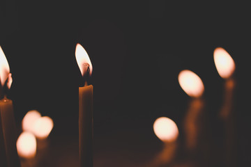 soft focus candle surrounded by other candles with fire in unfocused bokeh effect in black darkness church environment, religion concept photography wallpaper pattern with empty copy space