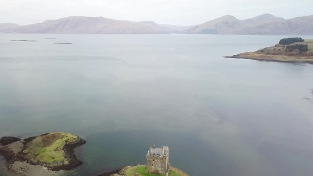 Aerial pull away reveal of the beautiful and historical Castle Stalker, situated in the picturesque Loch Laich in Scotland, UK