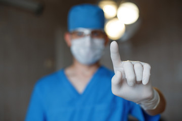 Young doctor in special blue medical clothes in a protective mask with rubber glasses is standing...