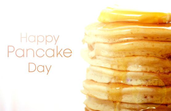 Stack of pancakes closeup, with drizzling honey syrup, with Happy Pancake Day text and lens flare.