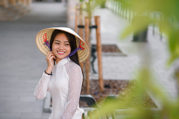 Fototapeta premium Close up portrait of pretty asian girl dressed in Ao Dai dress wearing vietnamese conical hat.