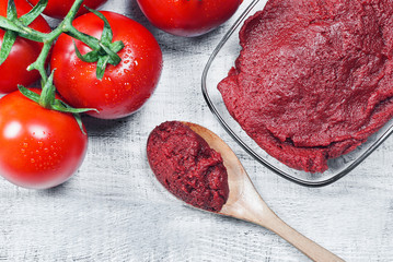 Tomato Paste in wooden spoon and ripe fresh grape tomatoes on wooden background. Cherry tomatoes. Tomato sauce ketchup food concept