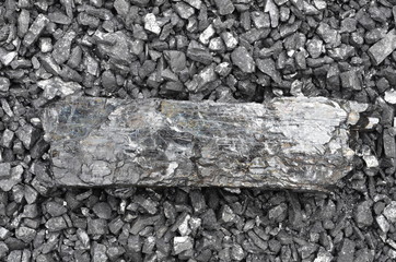 A large long piece of coal anthracite lies on the corner of a smaller fraction.