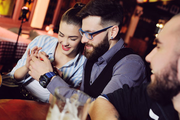 a group of friends - young guys and girls drinking beer, talking and smiling at the bar