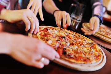 Hands taking pizza slices from wooden plate