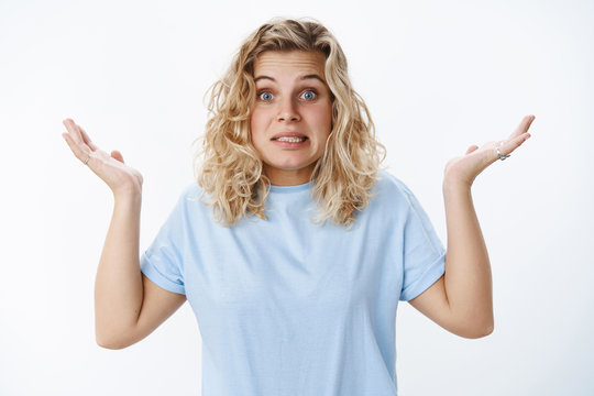 Yikes sorry my mistake. Portrait of awkward apologizing cute unaware and confused european blond female with blue eyes saying oops and grimacing as raising hands in clueless gesture over white wall