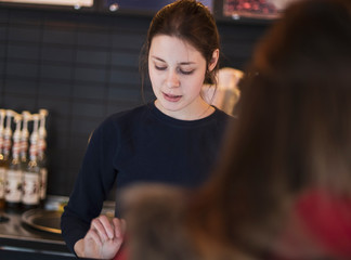 Attractive girl waiter, serves customers behind the counter. cake and people in cafe concept.