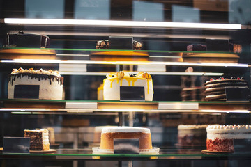 Obraz premium Showcase with a variety multicolored cakes and pastries. Glass fridge shelves with desserts in stylish dark interior of the cafe or restaurant