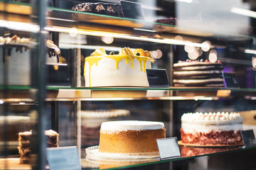 Showcase with sweets chocolate milk Strawberry fruit cakes for sale in cake shop. Different types Cake tray in showcase. Glass display at store bakery pastry shop.