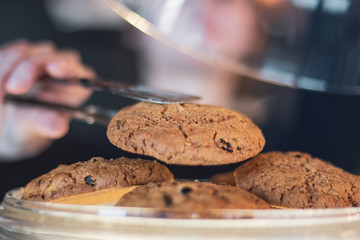 Female waiter holds cookie in the metal pinch which is taken from the confectionery shop for the ordering of the client. Ideal background for advertising a coffee shop, a cafe, a restaurant