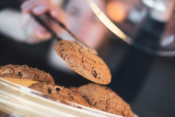 male hand open the glassware lid of the plate on which the delicious oatmeal cookies, in order for the buyer to choose a cake. The background for advertising a coffee shop, a cafe, a restaurant