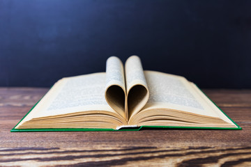 On the beautiful boards is an open book. Pages are folded in the shape of a heart. Black background. Day of knowledge. Hey. school. September 1. St. Valentine's Day. March 8. mothers Day. celebration