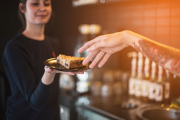 waiters are fun at work, the hand of a boy who stretches to a plate with a cake kept by a smiling girl waiter in a cafe.