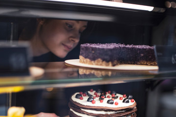 The girl waiter, seller putting delicious cake on the store showcase of the bakery house. cake and people in cafe concept.