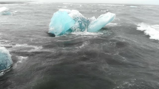 Drone flying out from a black sand beach to a blue glacial iceberg at the J&radic;&part;kuls&radic;&deg;rl&radic;&ge;n Glacier Lagoon in Iceland