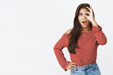 Waist-up shot of surprised and amazed charming young teenage indian girl popping eyes at camera, making orb with fingers and peeking through it astonished, open mouth from amusement