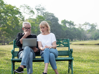 Senior man and woman couple connected on laptop computer in a park on a sunny day. relax in the forest spring summer time. free time, lifestyle retirement grandparents concept.
