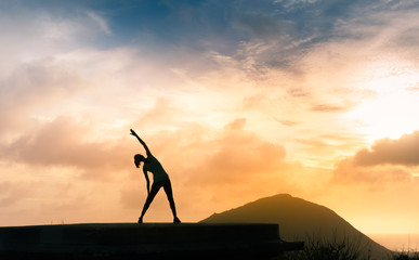 Woman doing stretching warm up exercise outdoors against a beautiful sunset