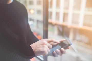 Side view of a man's hands pointing finger smart phone in interior.Rear view of business man hands busy using cell phone at office.Young male coworker typing on phone standing close windows.Flare