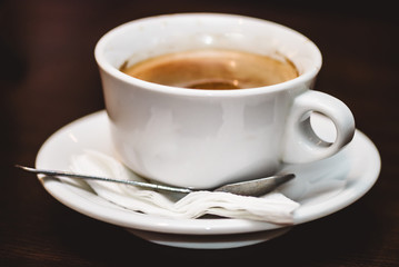 Close up view of a cup of strong frothy espresso coffee on a rough brown textured wooden surface. Selective focus macro shot with shallow DOF