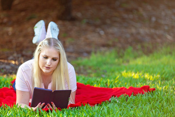 Young Blonde Girl Reading Kindle In Garden