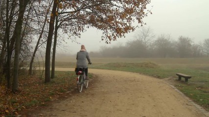 A cyclist passes by in a foggy city park.