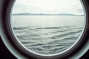 Round porthole on a cruise ship, interior view through the window on the coast and the sea, sunrise against the sea, close-up