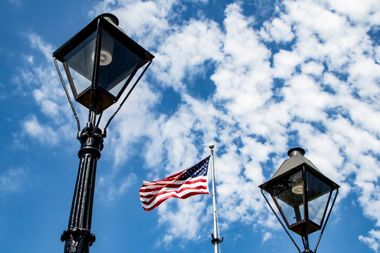 The American Flag Waves in the Breeze between Two, Antique, Iron Lampposts with the Blue Sky above at Jackson Square in the French Quarter of New Orleans, Louisiana, USA