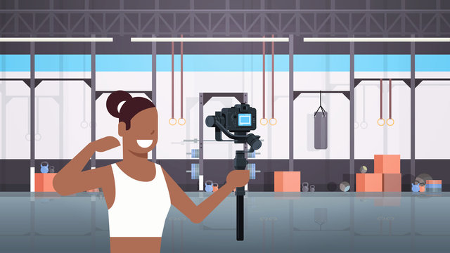 woman fitness blogger shooting selfie video african american girl in front of camera recording herself using gimbal stabilizer blogging concept modern gym interior horizontal